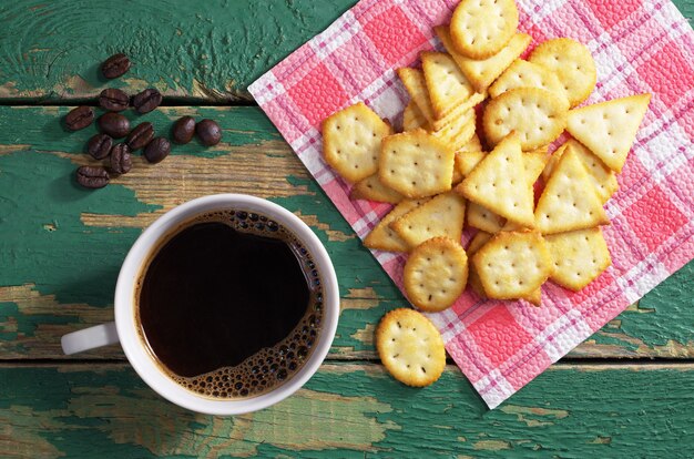 Tasse heißen Kaffee und Cracker mit Käsegeschmack auf grünem altem Holztisch, Draufsicht