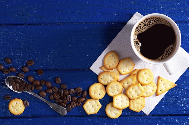 Tasse heißen Kaffee und Cracker mit Käsegeschmack zum Frühstück auf blauer Holztischplatte