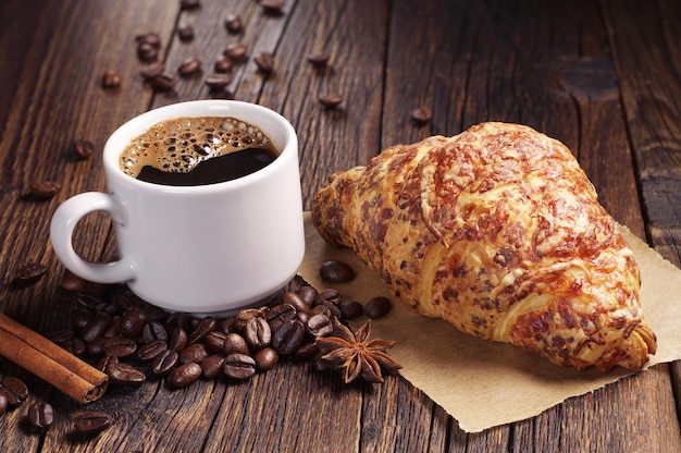 Tasse heißen Kaffee und Croissant mit Käse zum Frühstück auf einem dunklen Holztisch