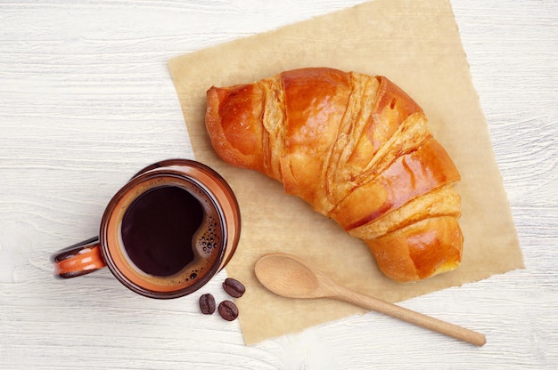 Tasse heißen Kaffee und Croissant zum Frühstück auf dem Tisch, Ansicht von oben