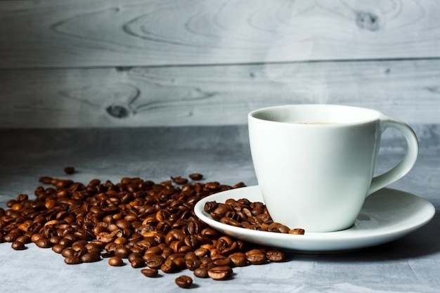 Tasse heißen Kaffee und Kaffeebohnen auf hellem Holzhintergrund