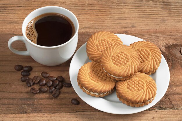 Tasse heißen Kaffee und Kekse mit Sahnefüllung auf altem Holztisch