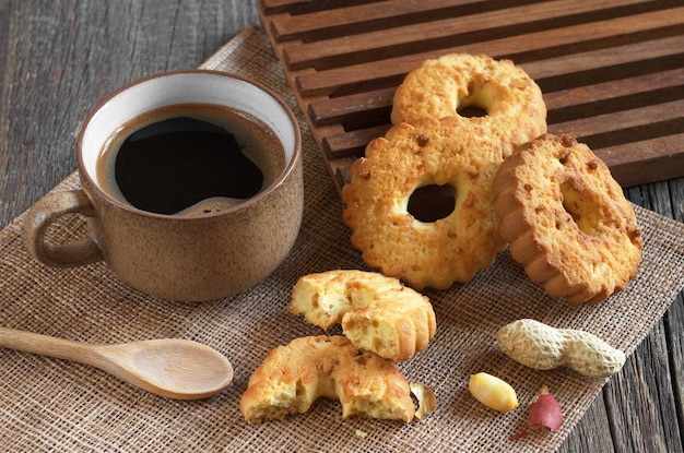 Tasse heißen Kaffee und Keksringe mit Nüssen auf altem Holztisch