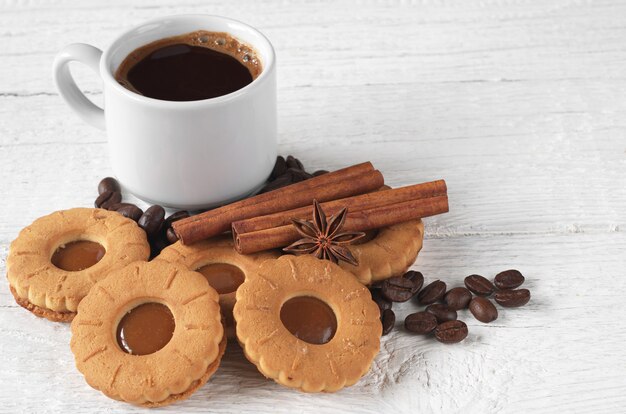 Tasse heißen Kaffee und leckerer Keks auf weißem Holzhintergrund