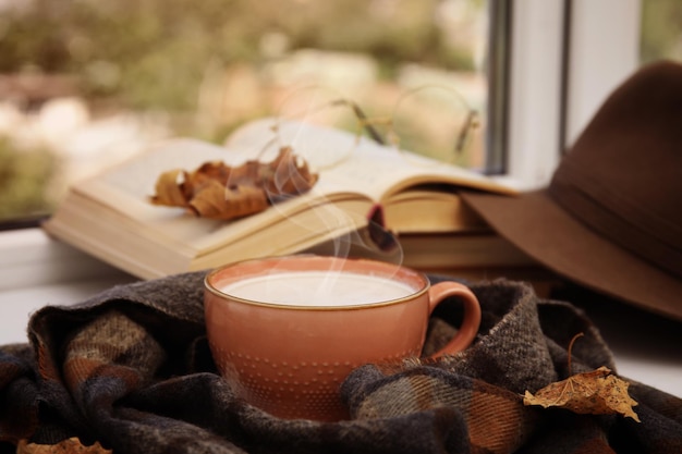 Tasse heißen Kaffee und warmen Schal auf der Fensterbank drinnen