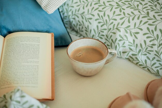 Foto tasse heißen kaffees, buch, weiche hausschuhe auf dem bett, frühstück im bett, gemütliches zuhause.