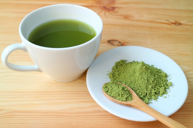 Tasse heißen Matcha-Grüntee mit einem Teller Matcha-Teepulver auf Holztisch