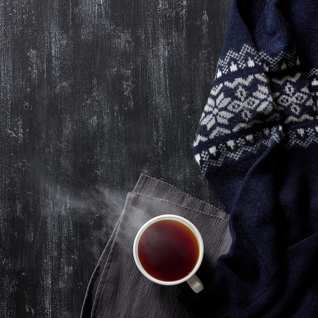 Tasse heißen Tee auf einem schwarzen hölzernen Hintergrund, warmer Winterpullover,