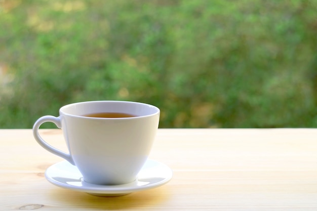 Tasse heißen Tee isoliert auf Tisch im Freien mit verschwommenem Laub im Hintergrund