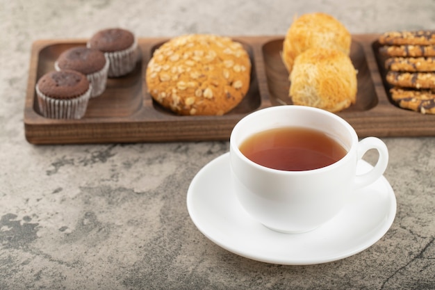 Tasse heißen Tee mit Teller mit verschiedenen Süßigkeiten auf dem Tisch.