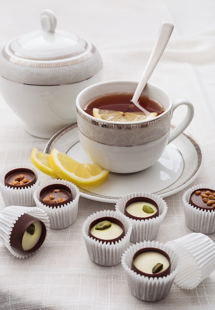 Tasse heißen Tee mit Zitrone und Praline auf Weiß