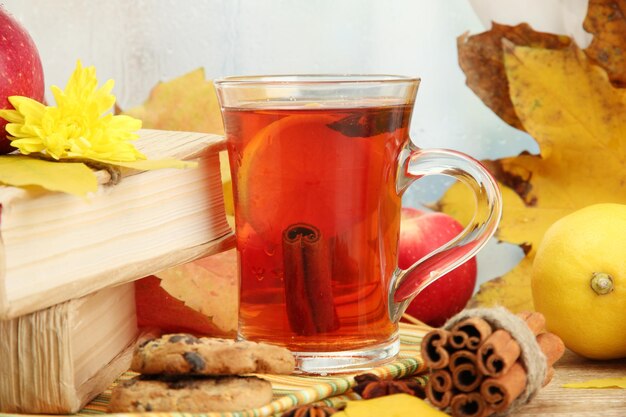 Tasse heißen Tee und Herbstlaub auf Holztisch