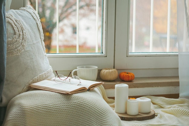 Tasse heißer Kakao auf einem Rattan-Tablett in der Nähe des Fensters ein Plaid ein Kissen Kürbisse Gemütliches Öko-Dekor für zu Hause Herbststimmung