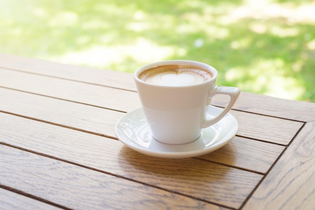 Tasse Kaffee am Morgen auf Holztisch Sonnenlicht und grünes Gras im Hintergrund