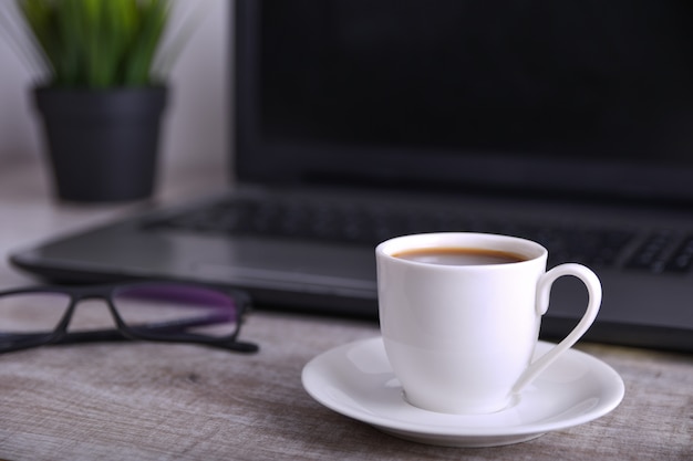 Tasse Kaffee auf Büro-Desktop mit Laptop, Computer auf Holztisch. Nahansicht