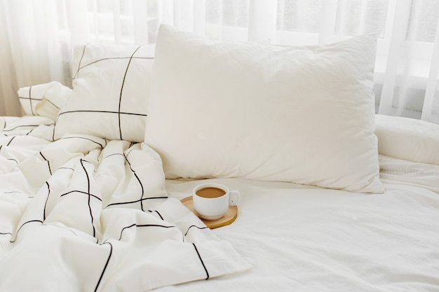 Foto tasse kaffee auf dem bett. weiße bettwäsche mit gestreifter decke und kissen.