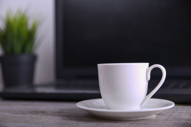 Tasse Kaffee auf dem Bürodesktop mit Laptop, Computer auf Holztisch. Close up, mit Platz für Ihren Text