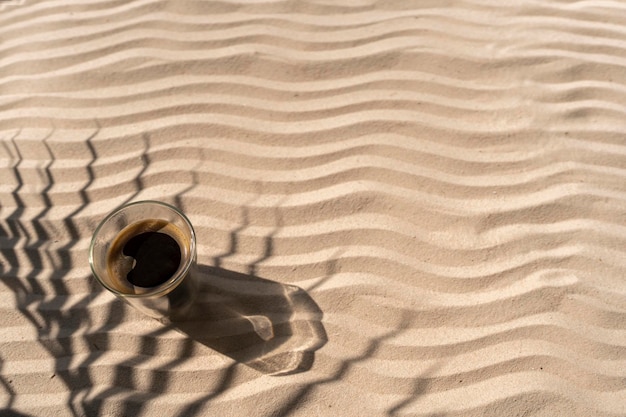 Tasse Kaffee auf einem wellenförmigen sandigen Hintergrund im Schatten der Palme