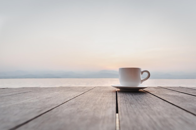 Tasse Kaffee auf Holzdeck bei Sonnenaufgang mit Flussberg im Hintergrund