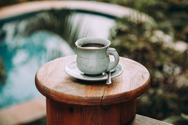 Tasse Kaffee auf Holztisch am Pool im tropischen Garten.