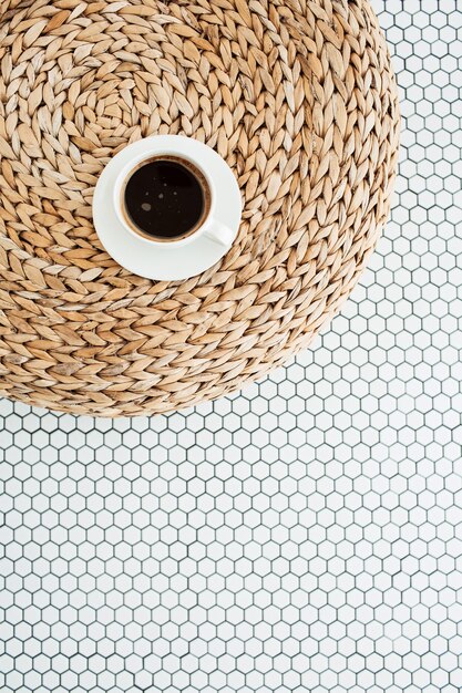 Tasse Kaffee auf Rattanstrohstoß auf weißer Mosaikfliese