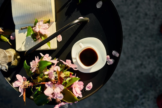 Foto tasse kaffee, blumen und notizbuch auf dem kleinen schwarzen tisch