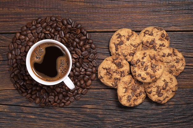 Tasse Kaffee, Bohnen in Kreisform und Kekse mit Schokolade auf dunklem Holztisch, Draufsicht