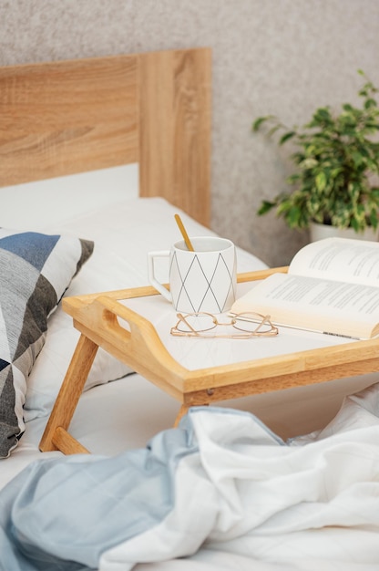 Tasse Kaffee, Buch und Gläser auf dem Bett mit weicher Decke im Innenbereich