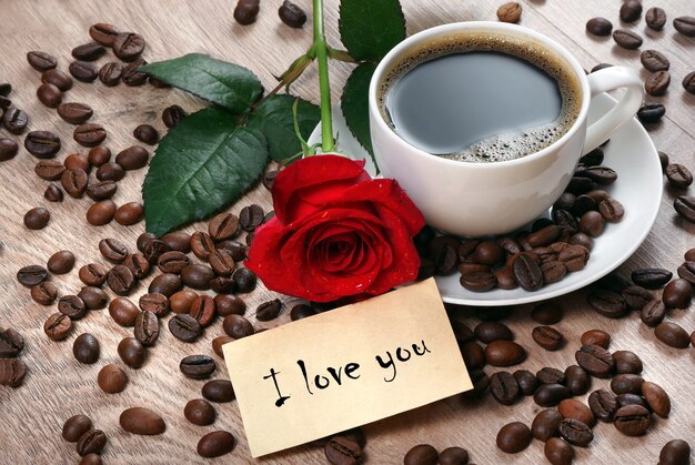 Tasse Kaffee, geröstete Kaffeebohnen und rote Rose auf einem Holztisch