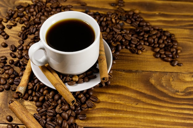Tasse Kaffee geröstete Kaffeebohnen und Zimtstangen auf Holztisch