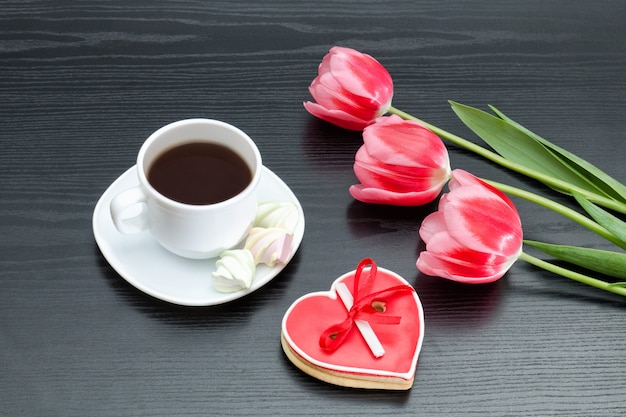 Tasse Kaffee, herzförmiges Lebkuchenplätzchen und rosa Tulpen
