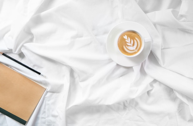Tasse Kaffee im Bett. Morgen flatlay im weißen Bett. Cappuccino und Morgenprogramm. Der Beginn des Tages