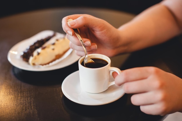 Tasse Kaffee in den Händen und ein süßes Dessert auf einem Teller hautnah