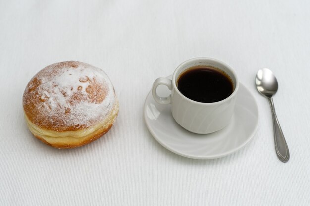 Tasse Kaffee in einer weißen Tasse mit einem Löffel und einem Donut auf einer hellen Oberfläche