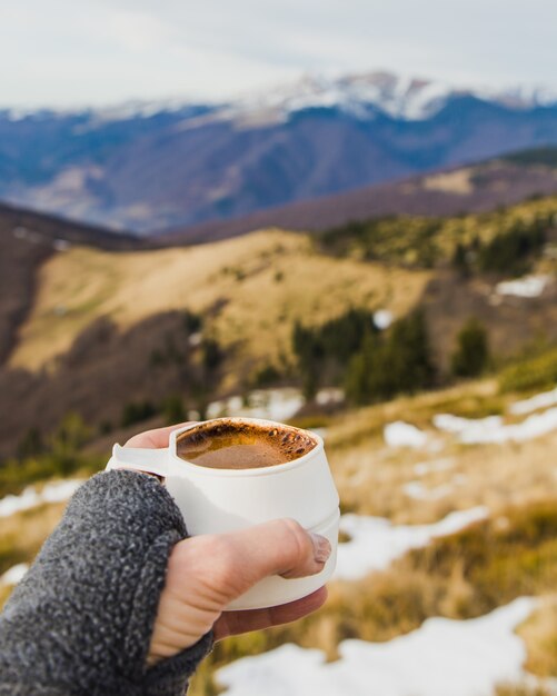 Tasse Kaffee in Frauenhänden in einer Berglandschaft