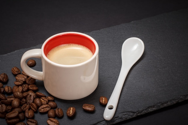 Tasse Kaffee, Kaffeebohnen und Löffel auf schwarzem Hintergrund. Ansicht von oben.