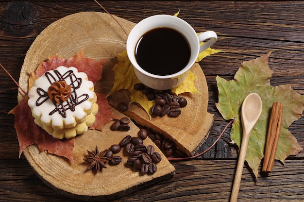 Tasse Kaffee, kleiner runder Kuchen und Herbstlaub auf altem Holzhintergrund