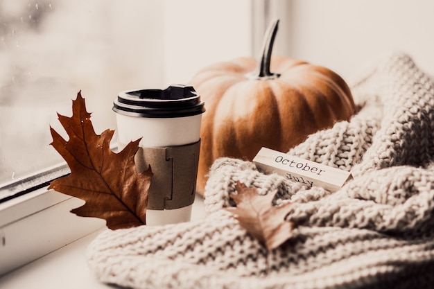 Tasse Kaffee, Kürbis, getrocknetes Herbstlaub am Fenster.