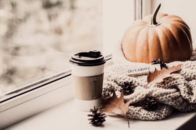 Tasse kaffee, kürbis, getrocknetes herbstlaub am fenster.