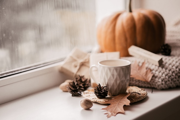 Tasse Kaffee, Kürbis, getrocknetes Herbstlaub am Fenster.