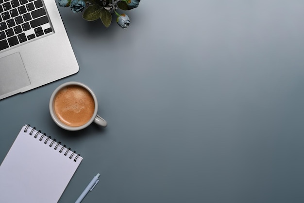 Tasse Kaffee, Laptop-Computer und Notizblock auf grauem Hintergrund.