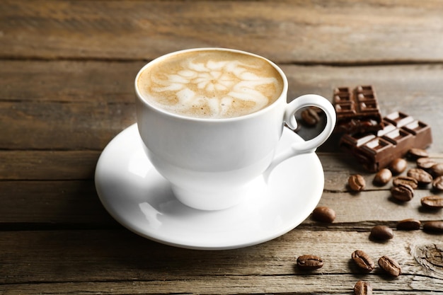 Tasse Kaffee Latte Art mit Körnern und Schokolade auf Holzhintergrund