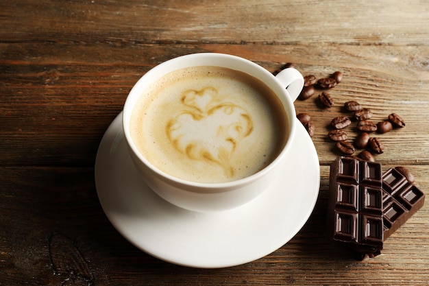 Tasse Kaffee Latte Art mit Körnern und Schokolade auf Holzhintergrund