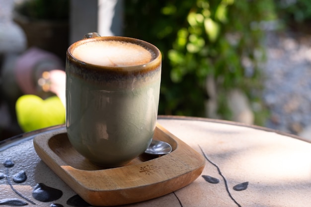 Tasse Kaffee Latte in grünem Poesiebecher auf altem Holzhintergrund in der Morgensonne