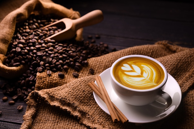 Tasse Kaffee Latte und Kaffeebohnen im Leinwandsack auf altem hölzernem Hintergrund