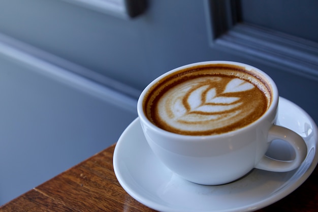 Tasse Kaffee Lattekunst auf dem hölzernen Schreibtisch