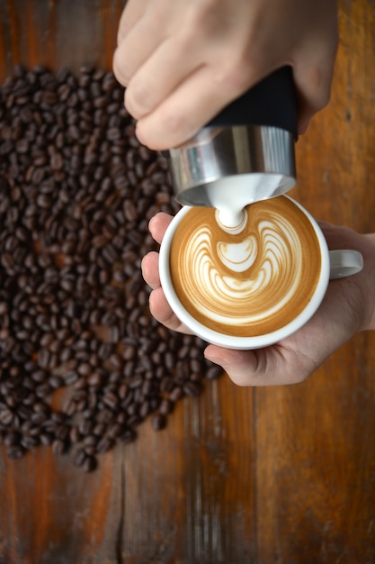 Tasse Kaffee Lattekunst, die durch barista auf altem hölzernem Hintergrund macht.