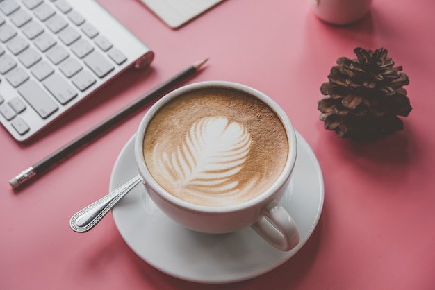 Tasse Kaffee Lattekunst Herzform mit Bürowerkzeugen auf rosa Tabelle