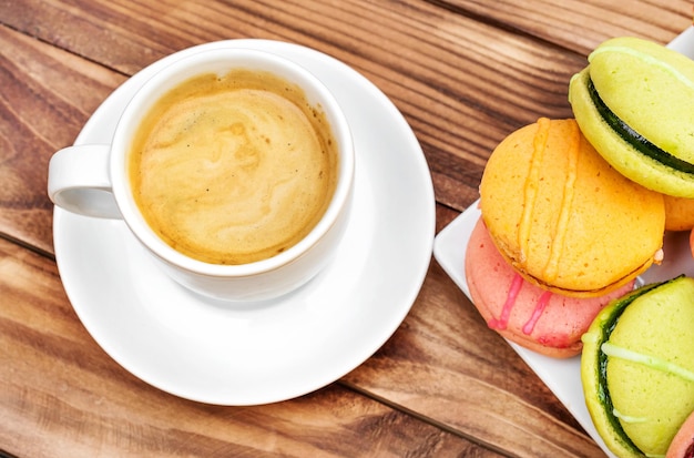 Tasse Kaffee mit bunten Makronen auf der Draufsicht des Holztischs