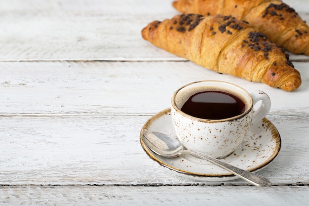 Tasse Kaffee mit Croissants auf einem weißen Holztisch, köstliches Gebäck, rustikal, Handwerk